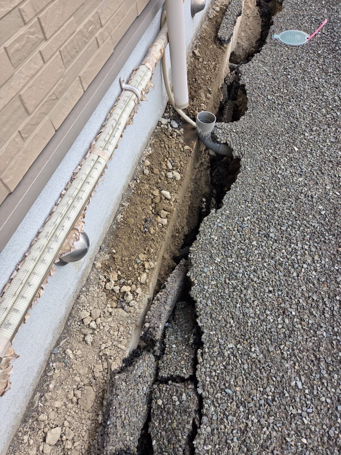 建物の外壁沿いの地面が割れ、配管が見えている様子